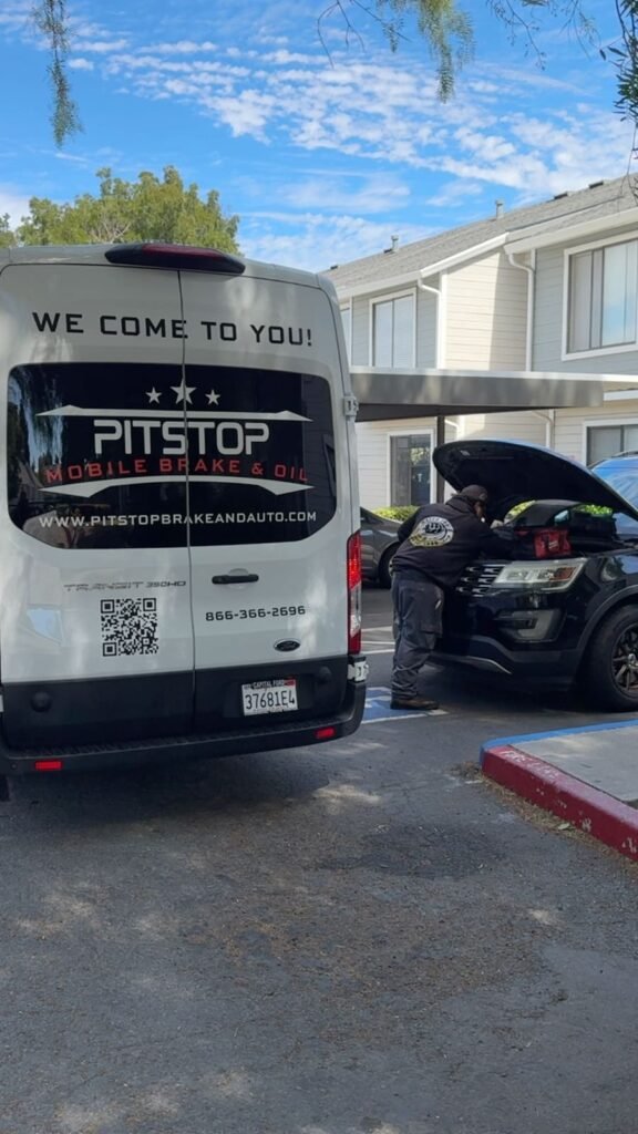 PitStop mobile mechanic technician working under the hood of a black Ford Explorer beside the service van at an apartment complex in the East Bay