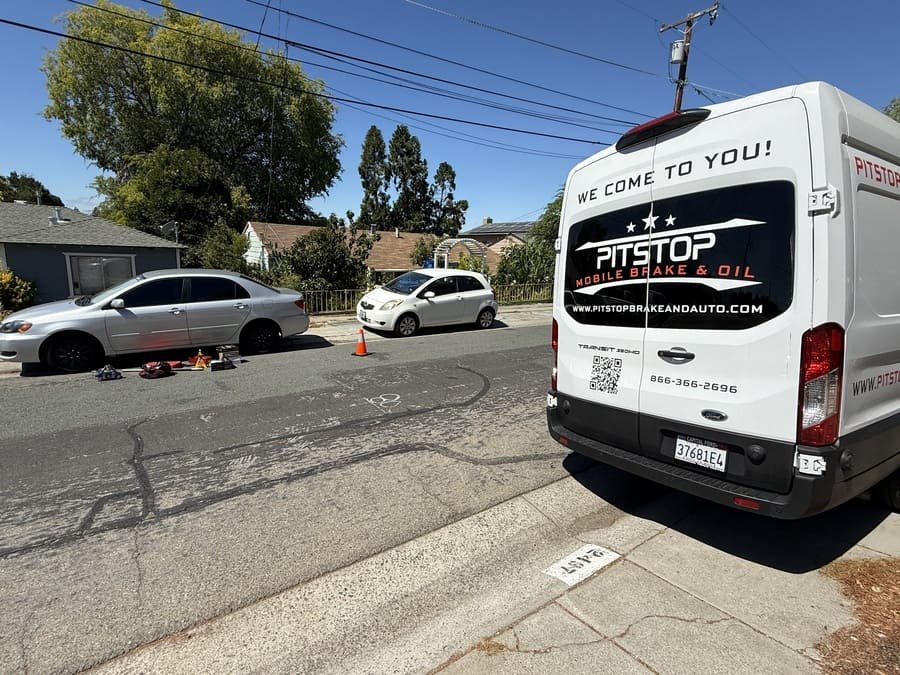 PitStop Mobile Mechanic service van parked on a residential street in Alameda County while a technician replaces brakes on a Toyota Corolla at the kerbside